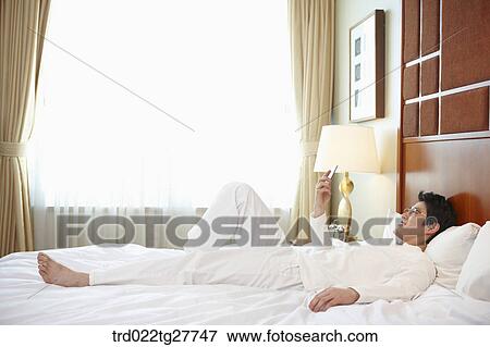 Stock Photo - man checking the mobile phone lying on the bed. Fotosearch