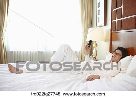 Stock Photo - man checking the mobile phone lying on the bed. Fotosearch