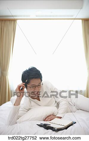 Stock Image - man checking the schedule lying down the bed. Fotosearch