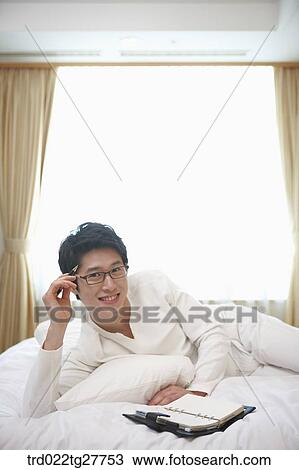 Stock Image - man checking the schedule lying down the bed. Fotosearch