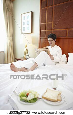 Stock Image - man reading a newspaper on the bed. Fotosearch