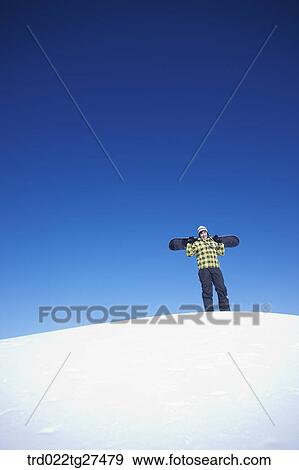 Stock Photo - man standing on the snow hill with a snow board. Fotosearch