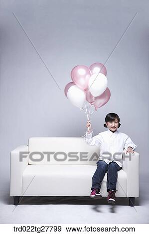 Stock Photo - children education girl holding balloons in her hand on sofa. Fotosearch