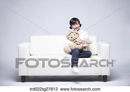 Stock Image - children education girl hugging teddy bear on couch. Fotosearch