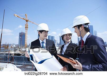 Picture - busineess people are going throught the blueprints at construction site. Fotosearch