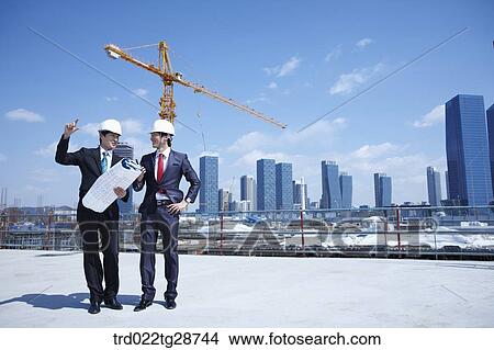 busineess people are going throught the blueprints at construction site View Large Photo Image Picture - busineess people are going throught the blueprints at construction site. Fotosearch