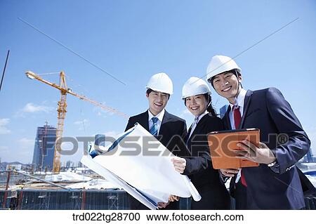 Stock Image - busineess people are going throught the blueprints at construction site. Fotosearch