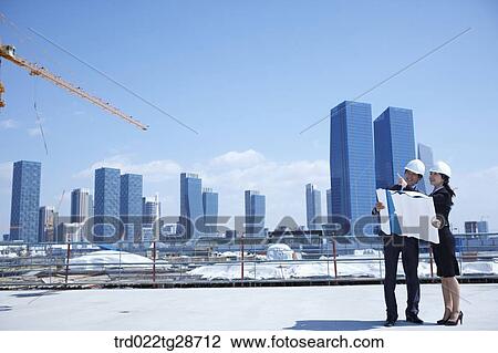 Stock Image - busineess people are going throught the blueprints at construction site. Fotosearch