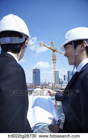 Stock Image - busineess people are going throught the blueprints at construction site. Fotosearch