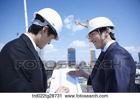 Stock Image - busineess people are going throught the blueprints at construction site. Fotosearch