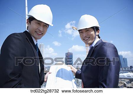 Stock Image - busineess people are going throught the blueprints at construction site. Fotosearch