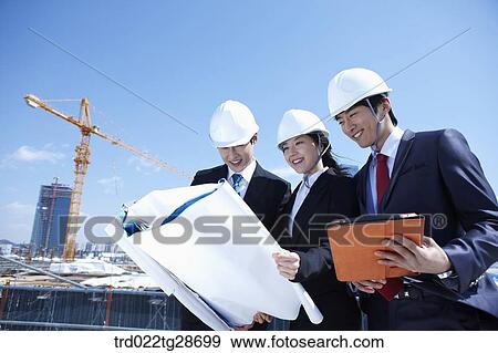 Stock Photo - busineess people are going throught the blueprints at construction site. Fotosearch