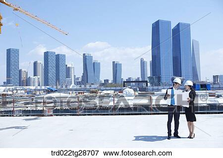 Stock Photo - busineess people are going throught the blueprints at construction site. Fotosearch