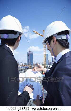 Stock Photo - busineess people are going throught the blueprints at construction site. Fotosearch