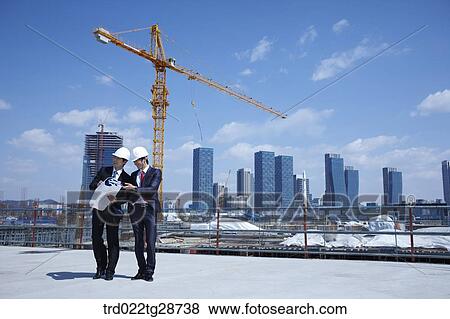 Stock Photo - busineess people are going throught the blueprints at construction site. Fotosearch