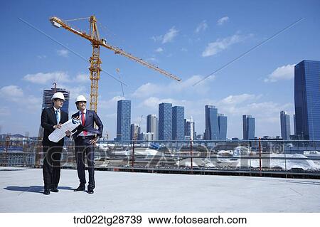 Stock Photo - busineess people are going throught the blueprints at construction site. Fotosearch