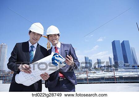 Stock Photo - busineess people are going throught the blueprints at construction site. Fotosearch