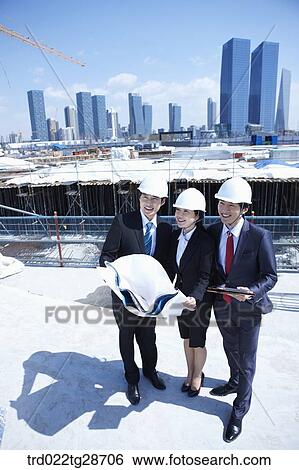Stock Photograph - busineess people are going throught the blueprints at construction site. Fotosearch