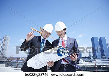 Stock Photograph - busineess people are going throught the blueprints at construction site. Fotosearch