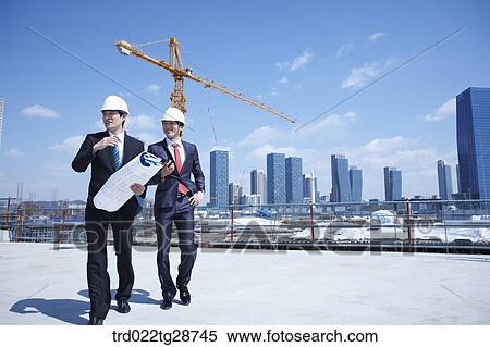 Stock Photography - busineess people are going throught the blueprints at construction site. Fotosearch