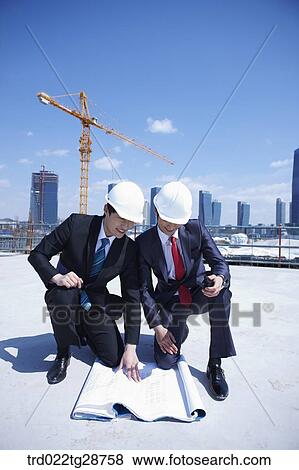 Stock Photo - business people are going throught the blueprints at construction site. Fotosearch