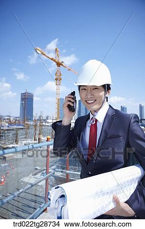Picture - businessman talking on the line holding blueprints. Fotosearch