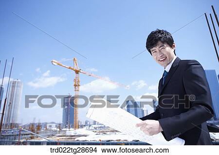 Picture - man is going through the blueprints at construction site. Fotosearch