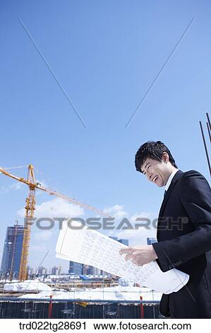 Stock Image - man is going through the blueprints at construction site. Fotosearch
