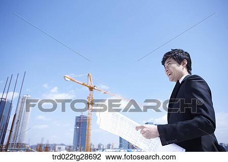 Stock Image - man is going through the blueprints at construction site. Fotosearch