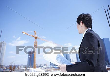 Stock Image - man is going through the blueprints at construction site. Fotosearch