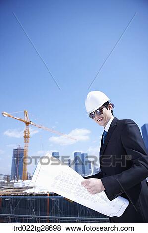 Stock Photo - man is going through the blueprints at construction site. Fotosearch