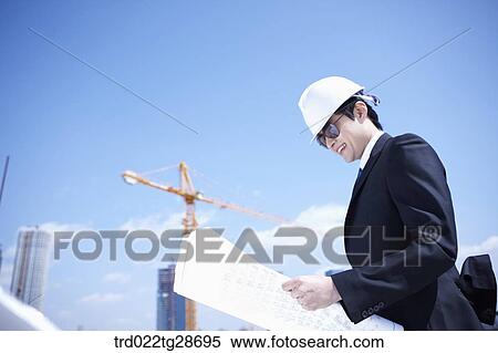 Stock Photography - man is going through the blueprints at construction site. Fotosearch