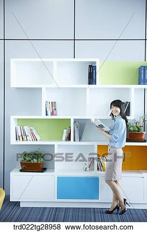 Stock Photo - woman reads book by the bookshelf. Fotosearch