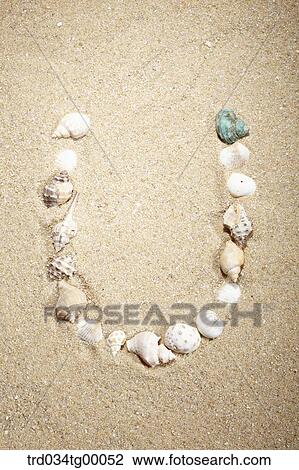 Stock Image - sea shells make letter of U on the sand. Fotosearch