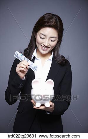 Stock Image - woman put money into piggy bank. Fotosearch