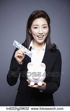 Stock Image - woman put money into piggy bank. Fotosearch