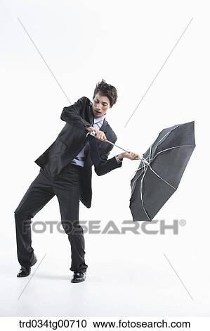 Stock Image - A man hit by the strong wind with an umbrella inside out. Fotosearch
