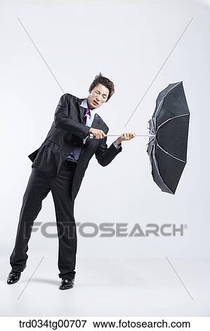 Stock Photo - A man hit by the strong wind with an umbrella inside out. Fotosearch