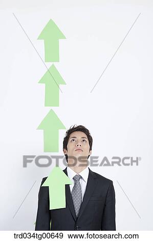 Stock Photo - A man looking upon rising green arrows. Fotosearch