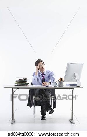 Stock Image - A thinking man while sitting on his desk. Fotosearch