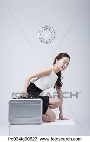 Stock Image - A woman about to run holding suitcase with clock background. Fotosearch