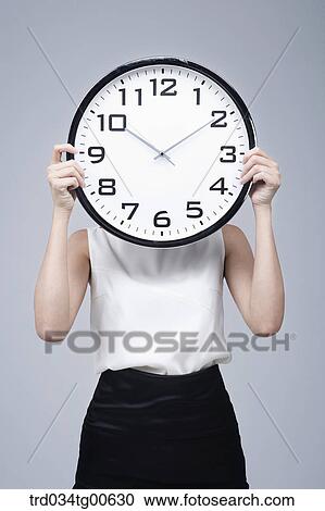 Stock Image - A woman holding the clock in front of her face. Fotosearch