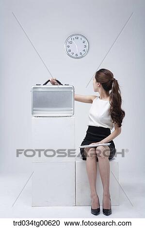 Stock Image - A woman looking back at clock and holding suitcase with keyboard. Fotosearch
