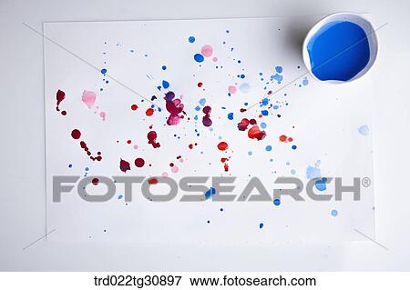 Stock Photo - A cup of blue paint and paints splattered on a paper. Fotosearch
