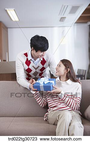 Stock Image - A man handing gift to a woman on the sofa. Fotosearch