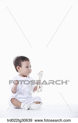 Stock Photo - Baby boy in white clothes with a toy giraffe. Fotosearch