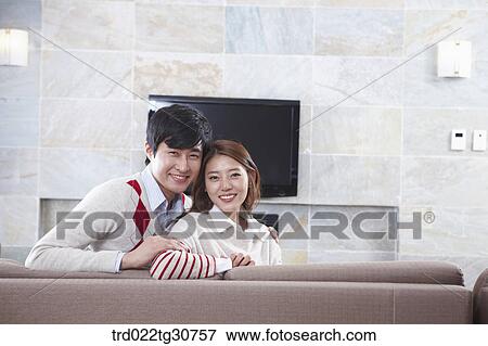Stock Photo - Happy couple on the sofa and a televison. Fotosearch