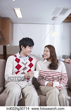 Happy couple sitting on a sofa with a cup View Large Photo Image Picture - Happy couple sitting on a sofa with a cup. Fotosearch