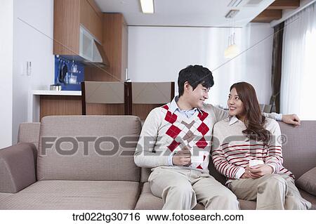 Stock Photograph - Happy couple sitting on a sofa with a cup. Fotosearch