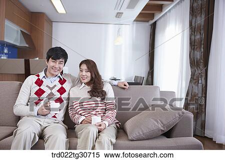 Stock Photography - Happy couple sitting on a sofa with a cup. Fotosearch
